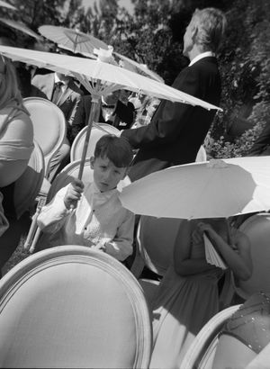 Group of people holding white parasols at an outdoor gathering in black and white.