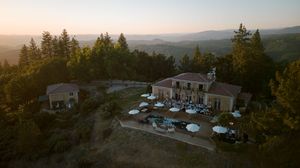 Panoramic sunset view of mountains and trees with buildings visible in the distance.