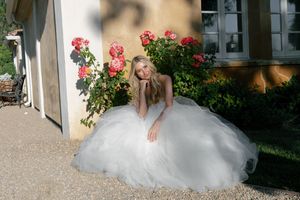 A bride in a flowing white wedding gown poses gracefully in a garden setting with blooming pink roses.
