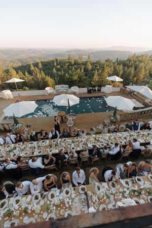 Aerial view of long wedding reception table setup with mountain landscape backdrop.