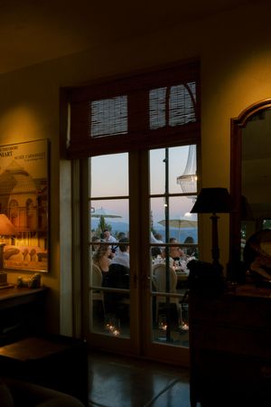 Warm interior view through French doors at sunset showing a restaurant dining area with silhouetted guests.