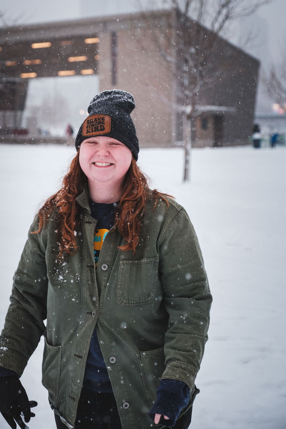Person enjoying a snowy winter day wearing a green jacket and winter hat in a snow-covered landscape.