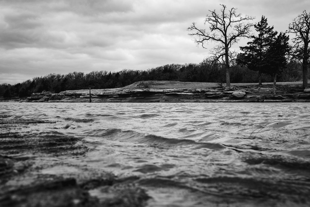 A dramatic black and white panoramic view of stormy waves crashing against a rocky coastline during rough weather.