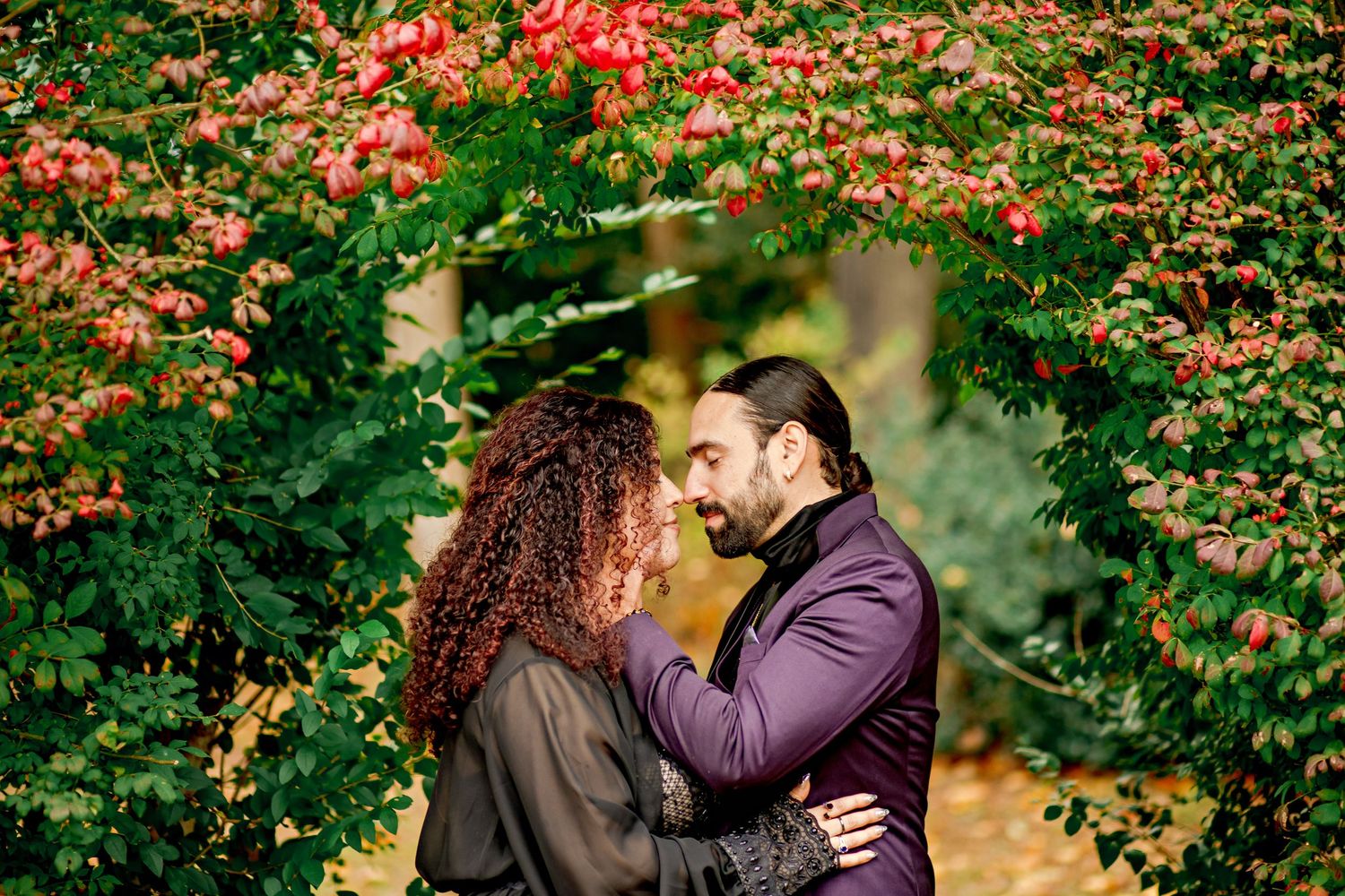 A couple embraces lovingly on a dirt path beside tall ornamental grasses on an overcast afternoon.