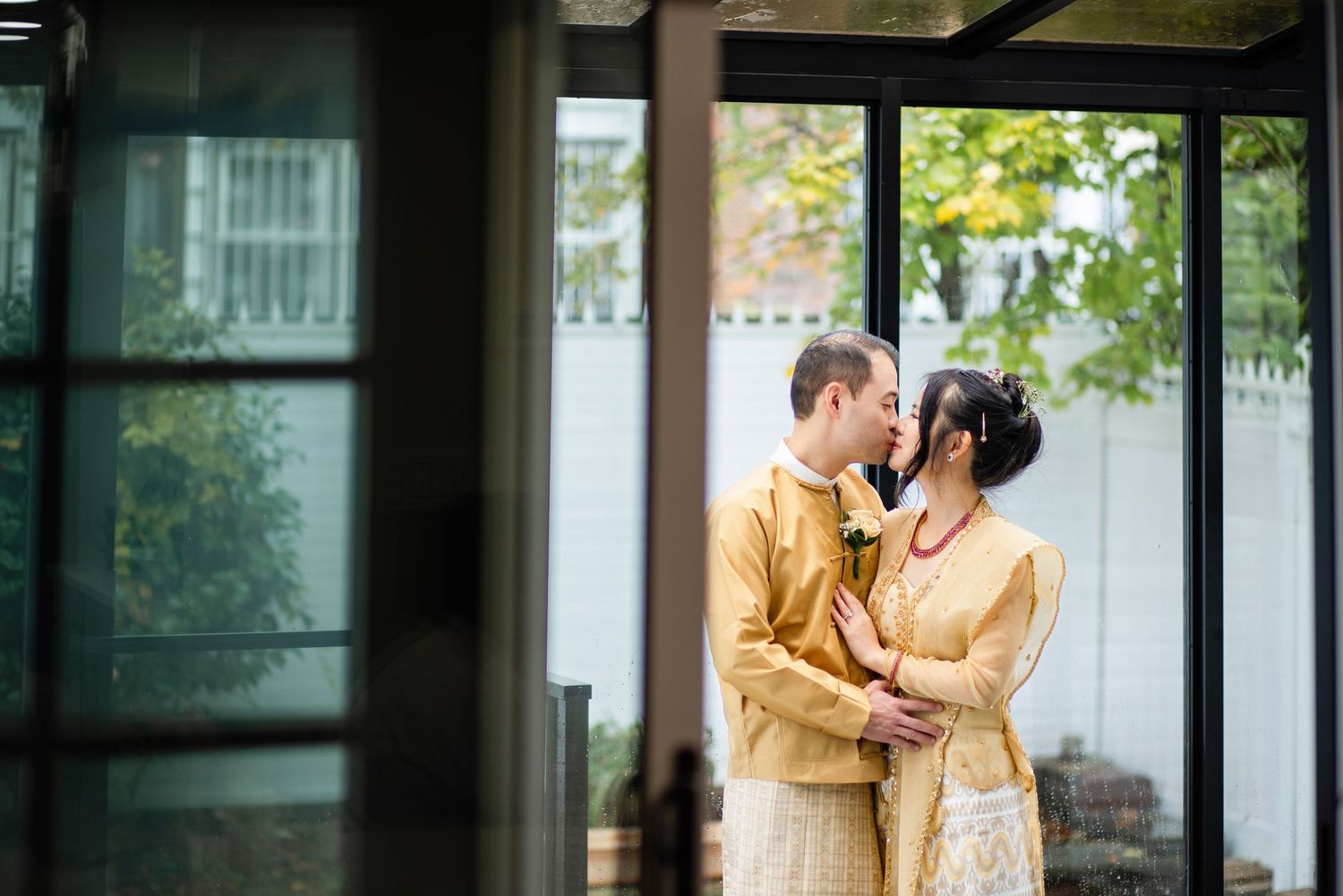 A couple embraces lovingly on a dirt path beside tall ornamental grasses on an overcast afternoon.