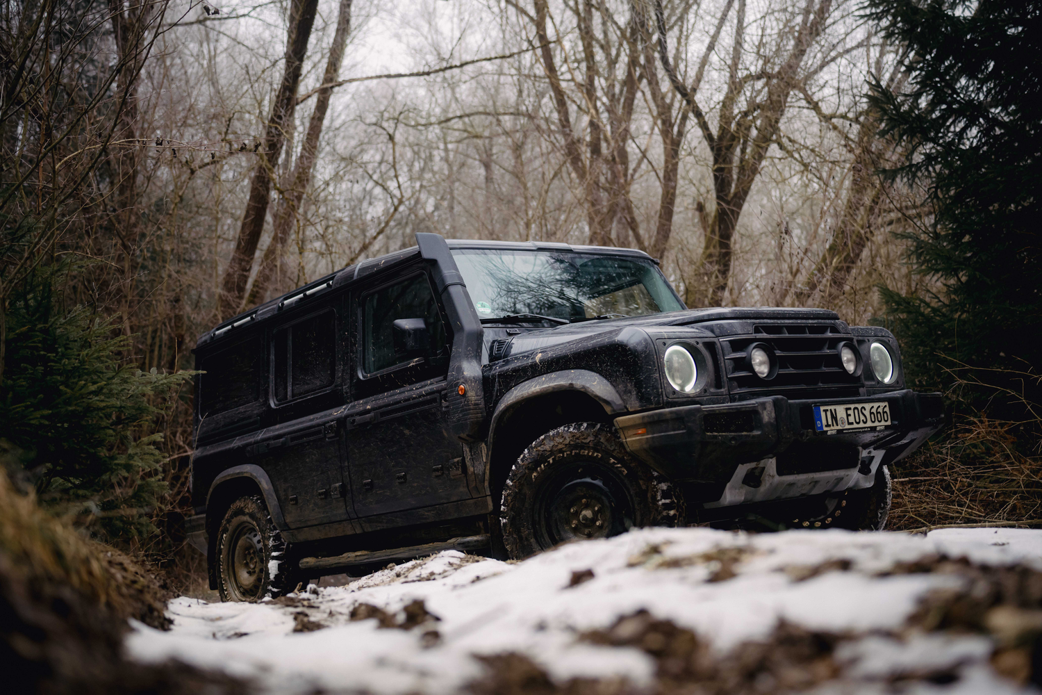 Black off-road vehicle navigating through a snowy forest trail during winter.