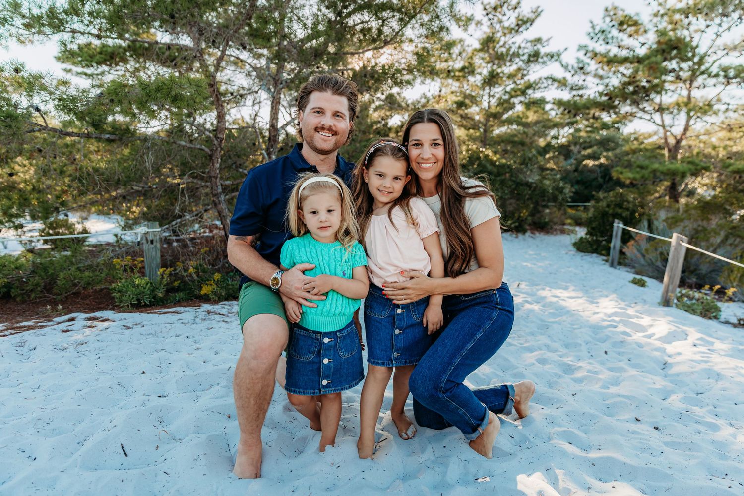 A family sits together on a white sandy beach during a sunset photo session.