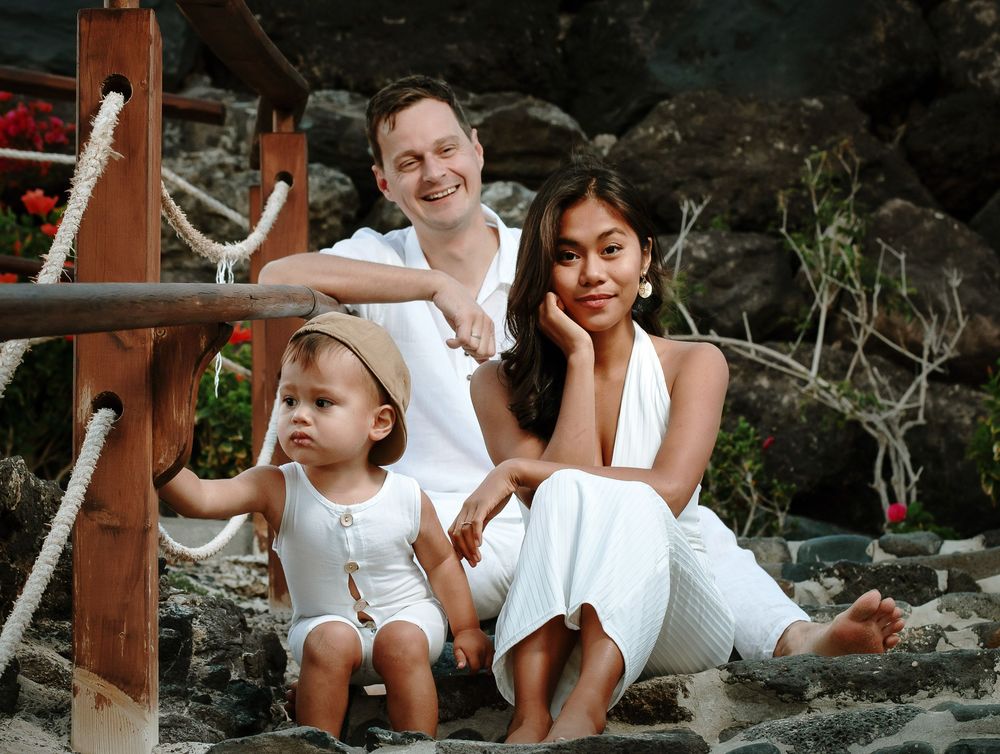 Family of three dressed in white posing on the dark volcanic rocks - Professional family photographer in Fuerteventura