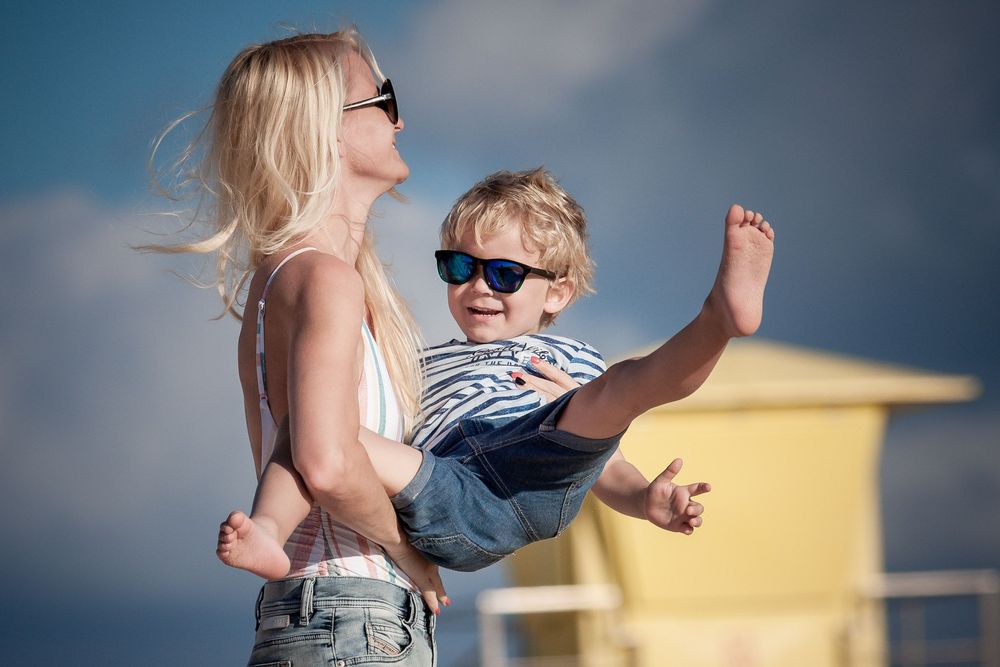 Mother holding her laughing son by a yellow lifeguard tower - Fun family lifestyle session at Grandes Playas, Corralejo