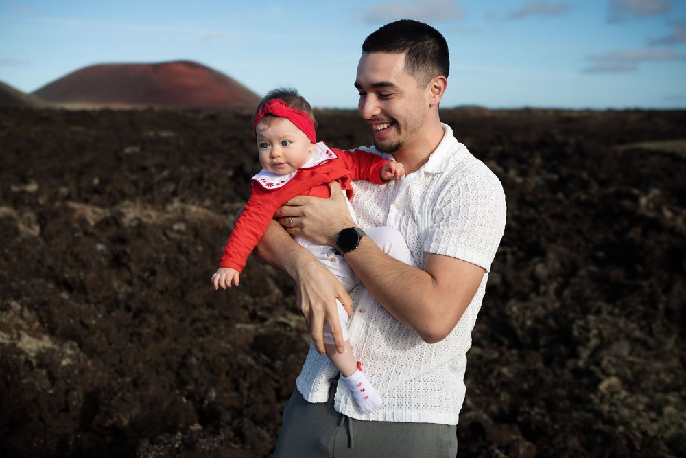 A parent and baby share joyful moments together against a scenic volcanic landscape backdrop in La Geria, Lanzarote
