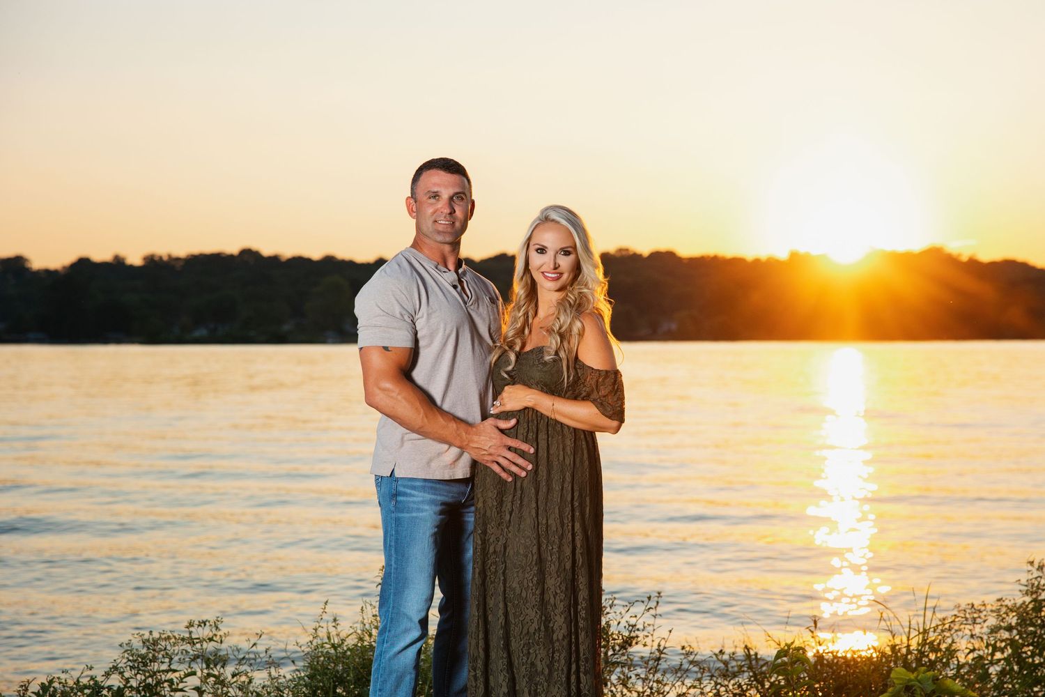 Expectant couple stands silhouetted against a golden sunset on a lake shore.  Hendersonville maternity photography.  Professional maternity.