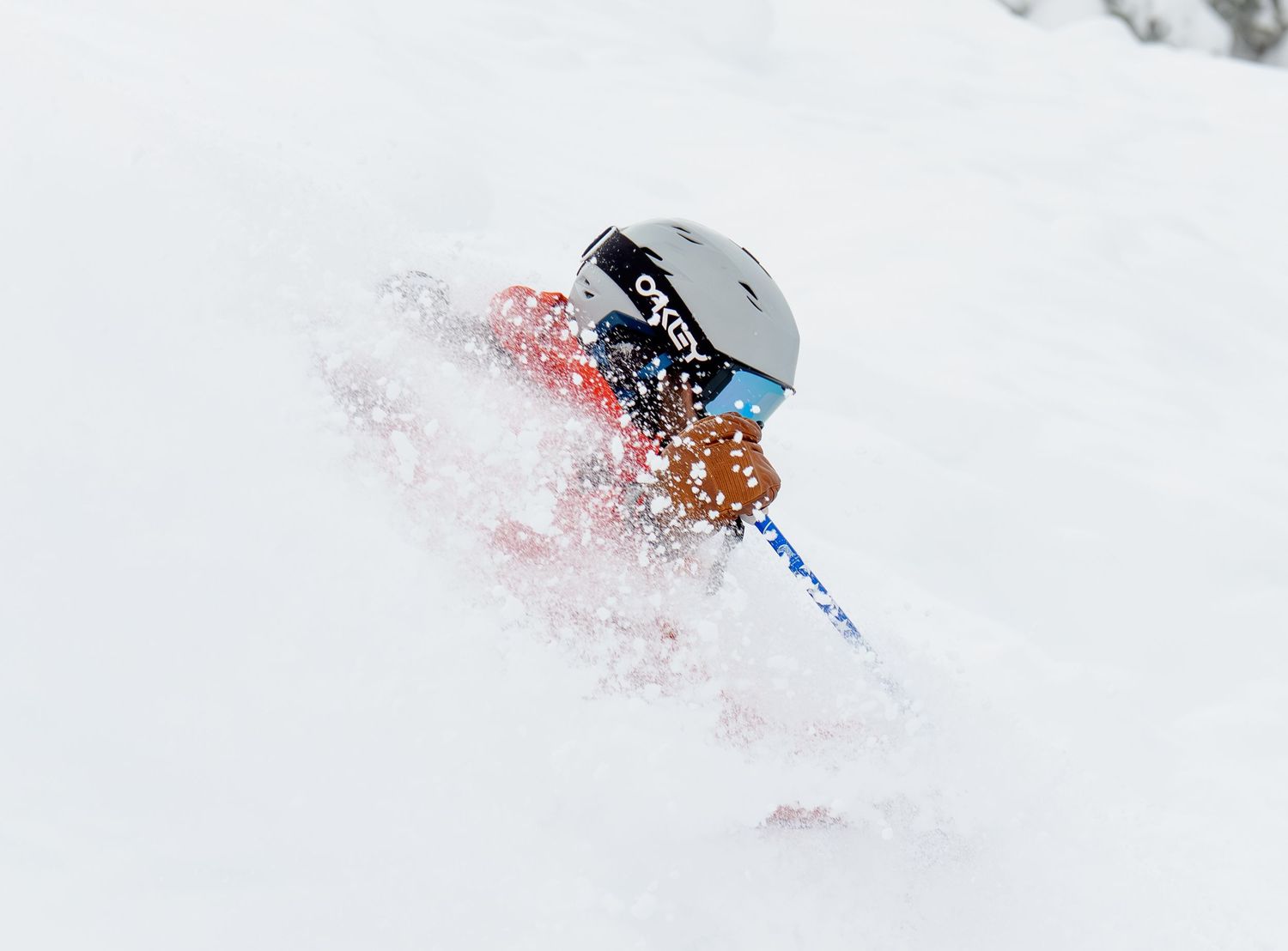 A skier creates a dramatic spray of powder snow while carving down a steep slope on a bright winter day.