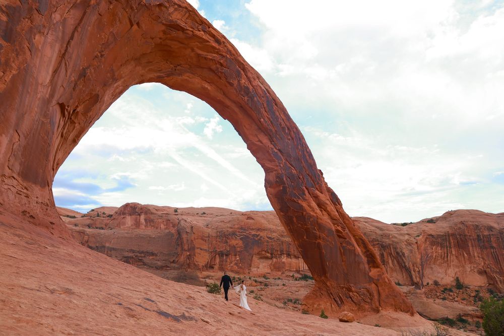 A panoramic view of a natural sandstone arch formation in a desert landscape under blue skies.