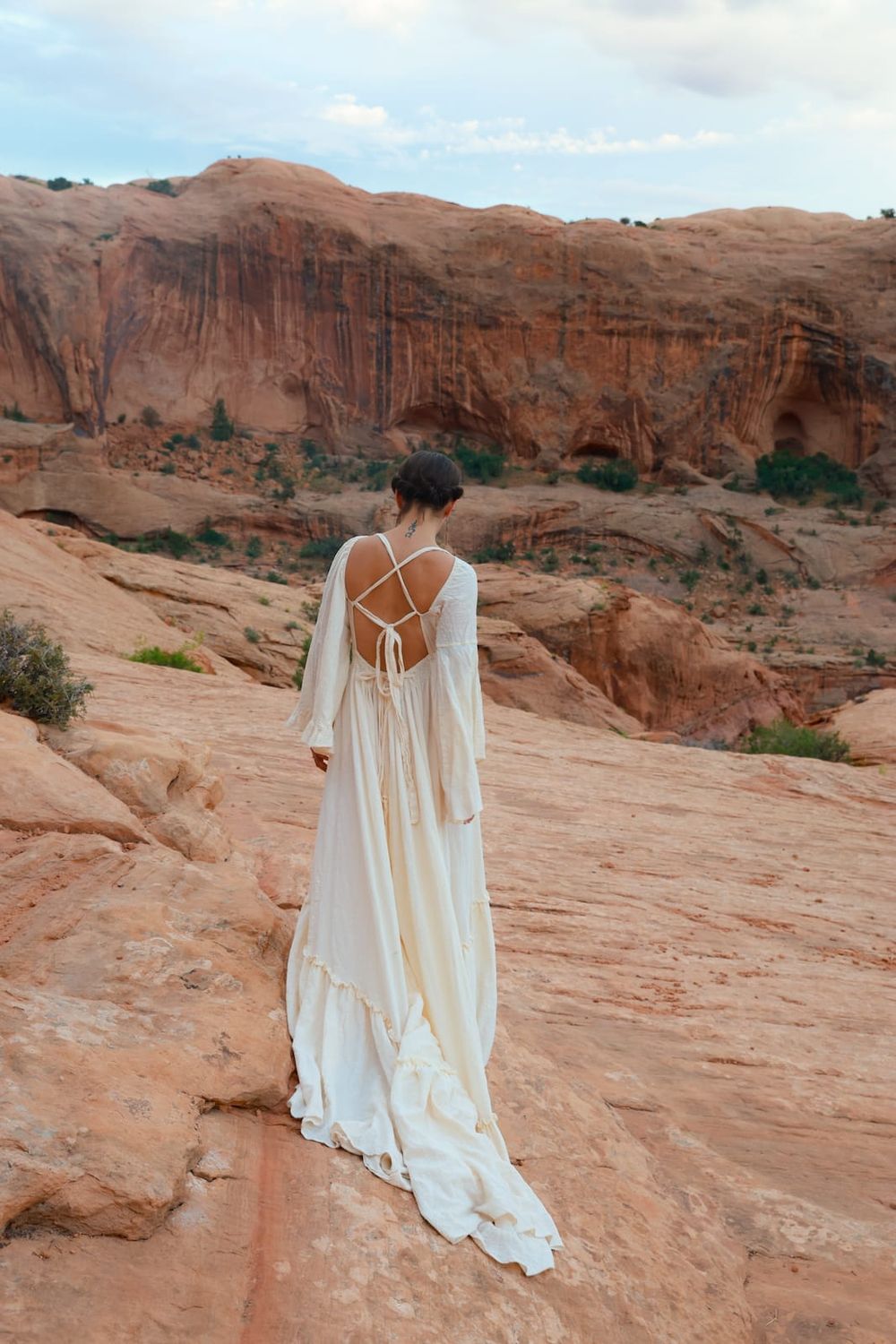 Two figures in flowing white dresses stand gracefully against the backdrop of red rock formations in Arches National Park.