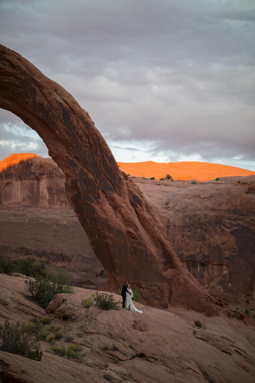 A series of dramatic red rock formations in Arches National Park at sunset with stormy clouds overhead.