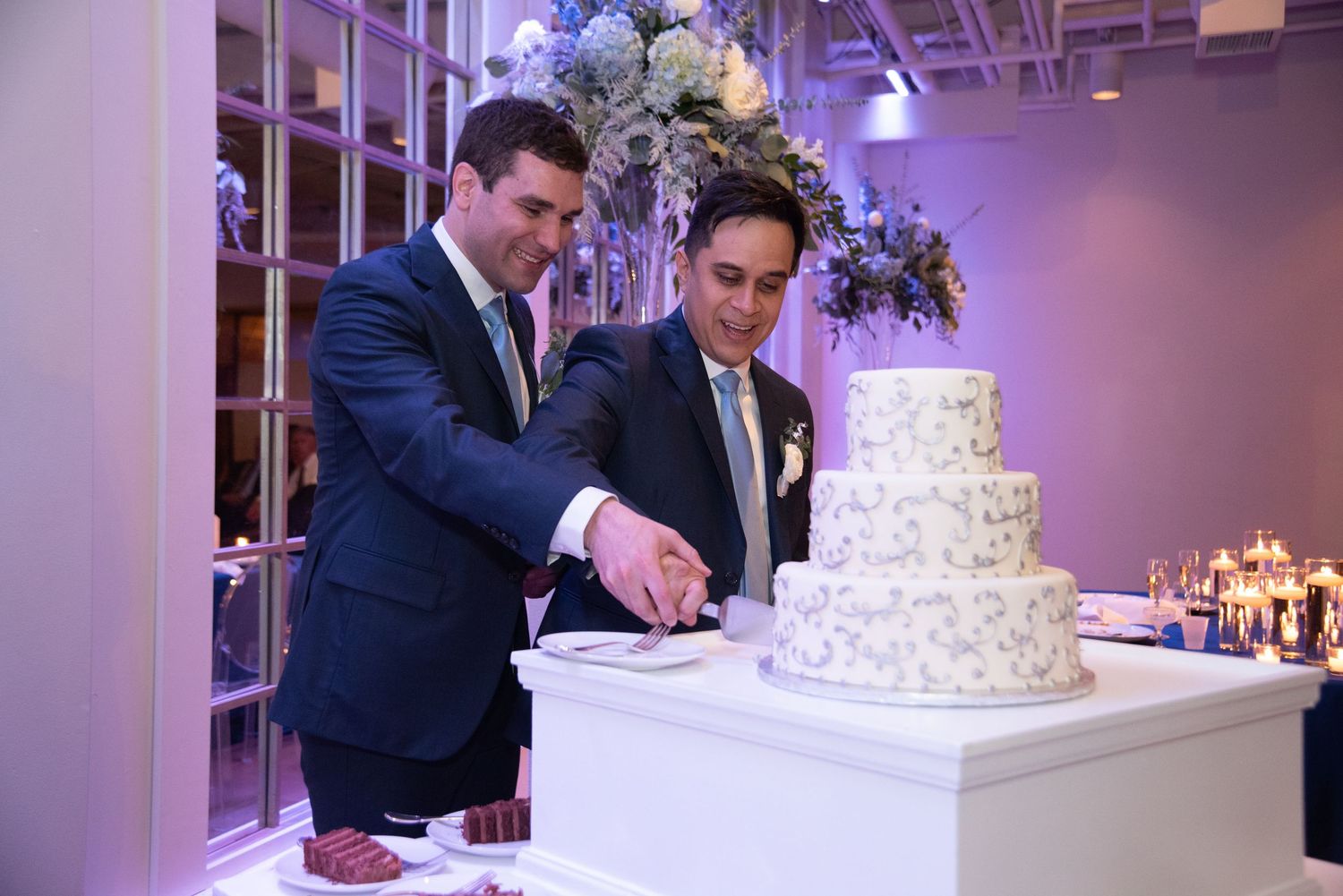 An elegant white wedding cake displayed at a reception with purple lighting.