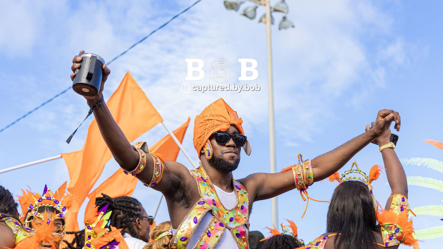 A carnival reveler wearing a colorful costume and headwrap with arms raised while celebrating during Sugar Mas 54 Carnival in St. Kitts.