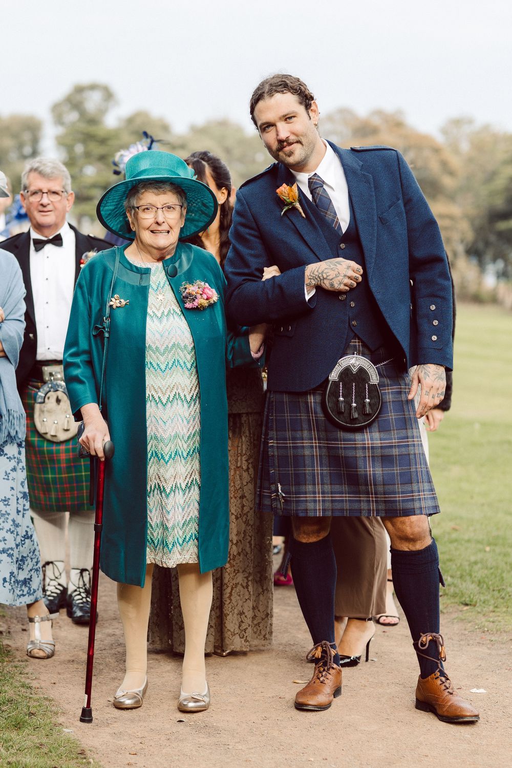 Wedding party members in traditional Scottish kilts and formal attire pose together outdoors.