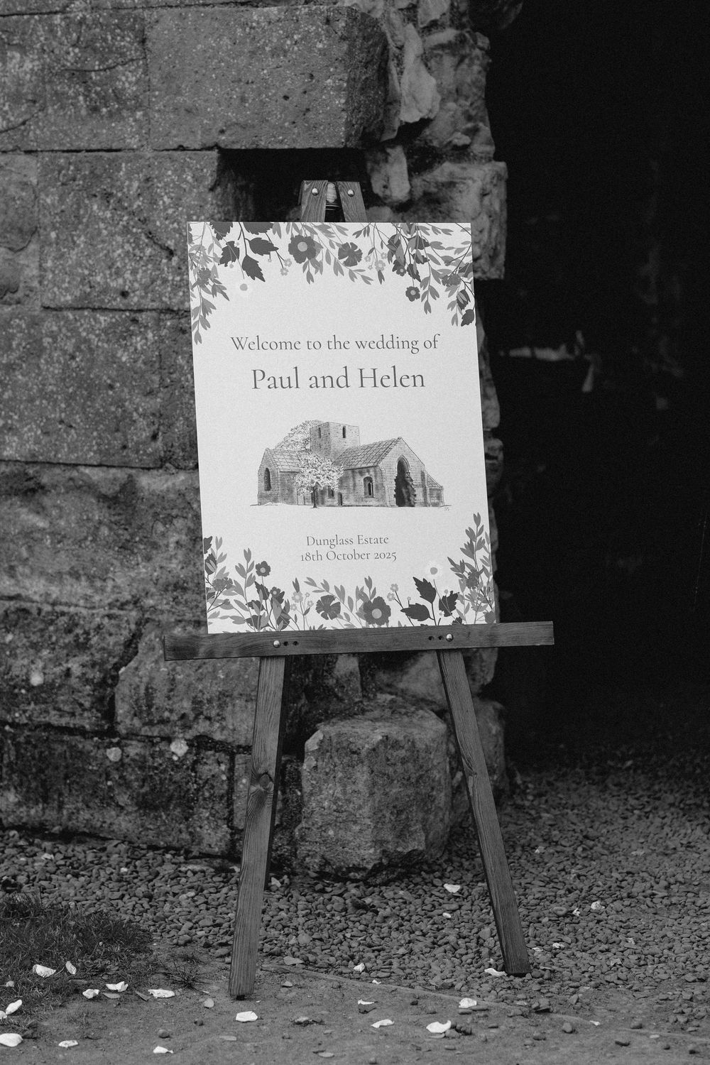 Wedding welcome signs displayed on wooden easels against a stone wall with floral designs.