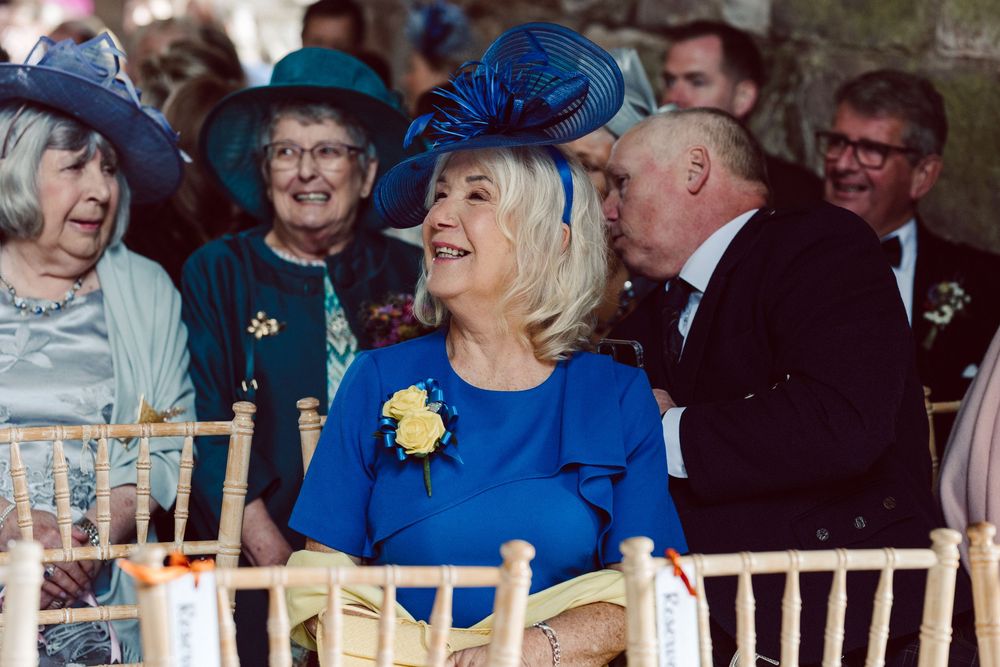 Wedding guests share joyful laughter while seated in white chairs during an outdoor ceremony.