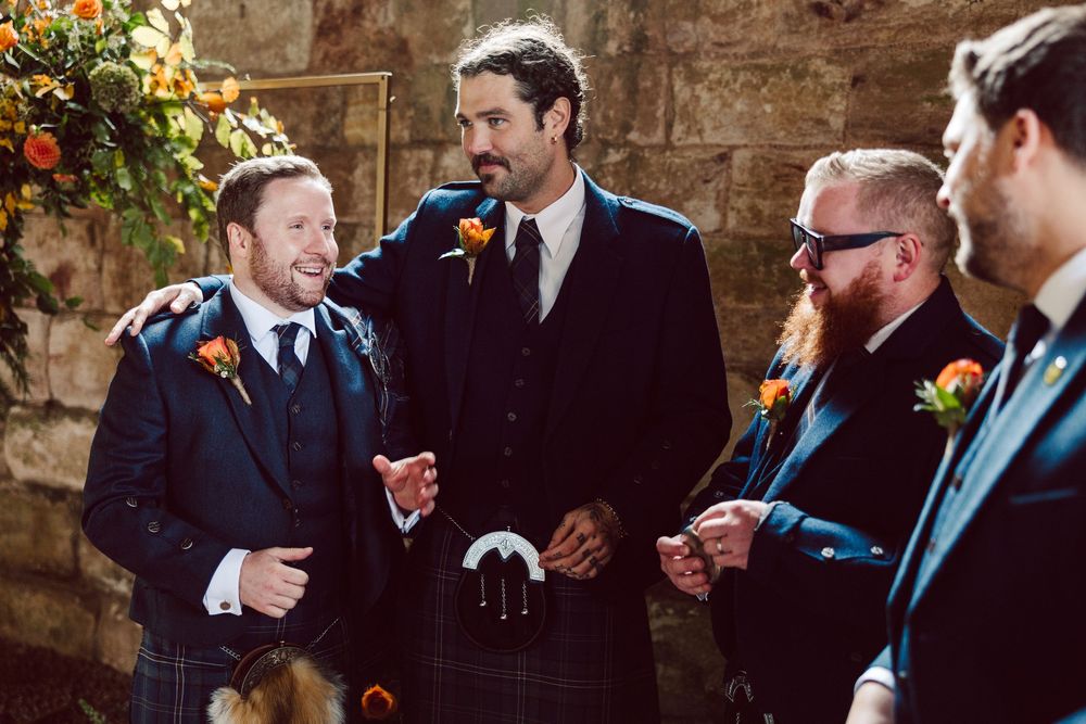 A group of wedding party members in formal attire share drinks and laughter together during a celebratory moment.