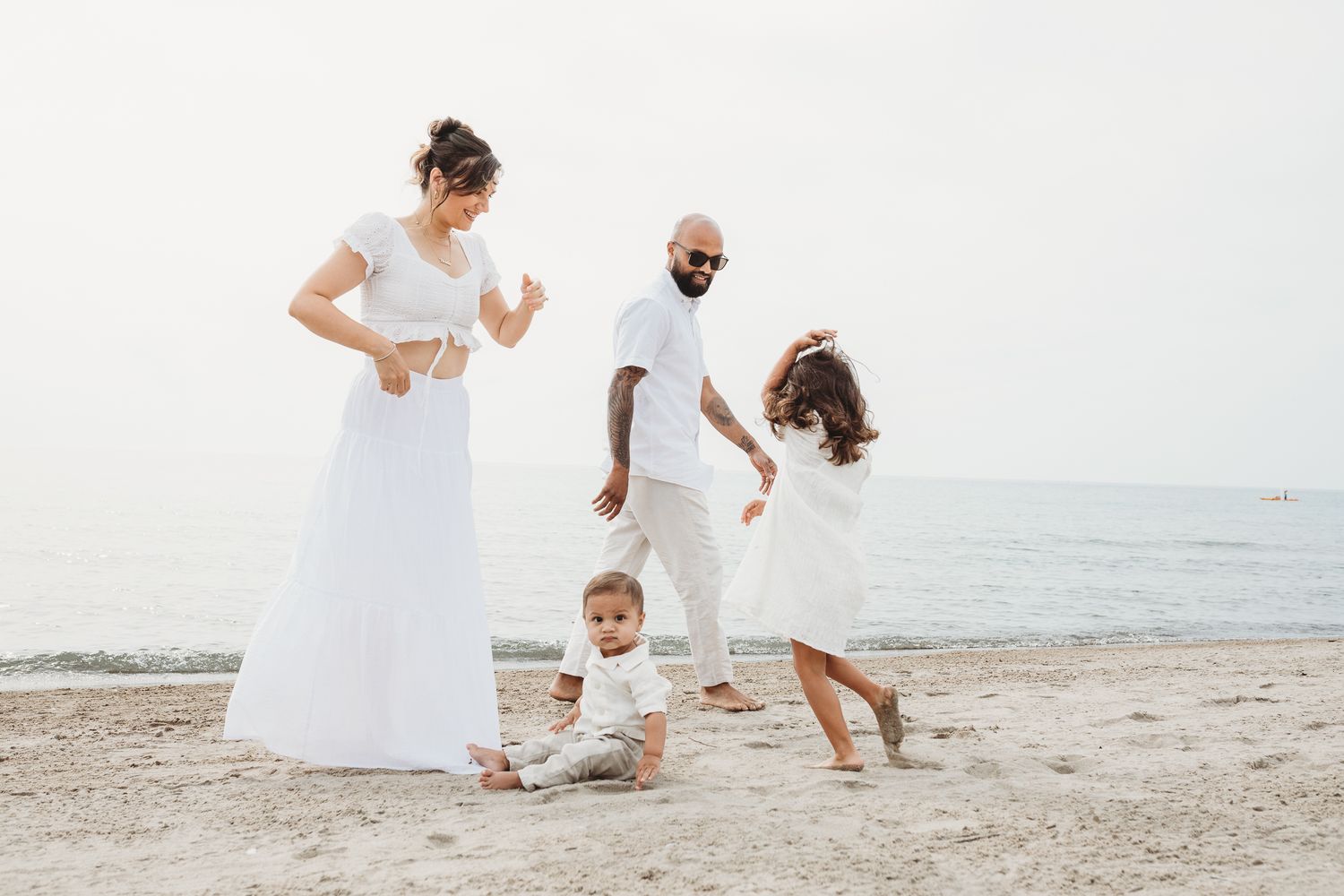 A family in white outfits dances together on a peaceful beach with the ocean in the background.