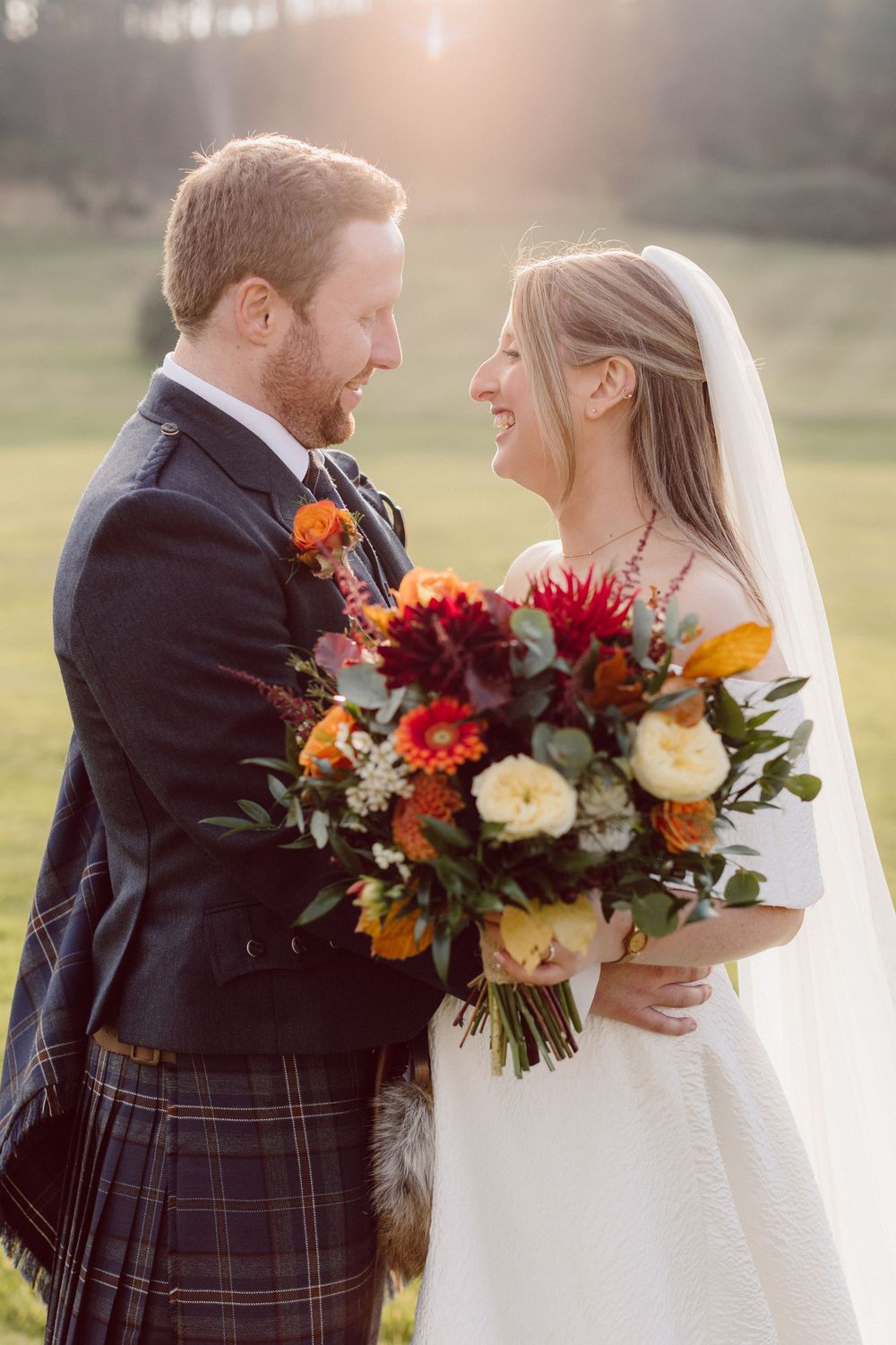 Intimate wedding portraits with couple in Scottish kilt and white dress holding vibrant fall floral bouquet.