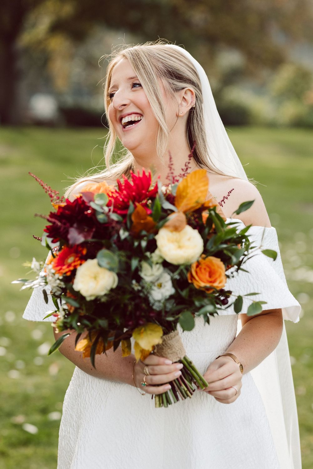 Close-up shots of a bride in white dress holding a vibrant fall-colored wedding bouquet with burgundy and orange flowers.