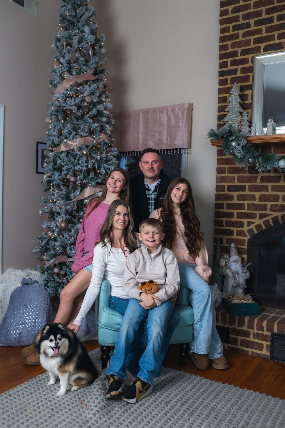 Family sits together on couch with dog during holiday season with decorated Christmas trees in background.