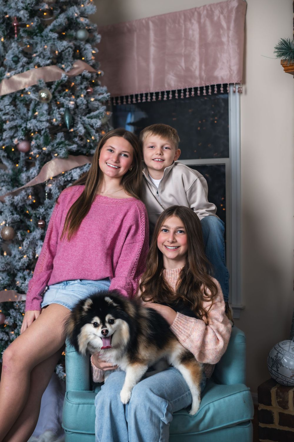 Family and their happy fluffy dog pose together on a teal couch with a decorated Christmas tree in the background.