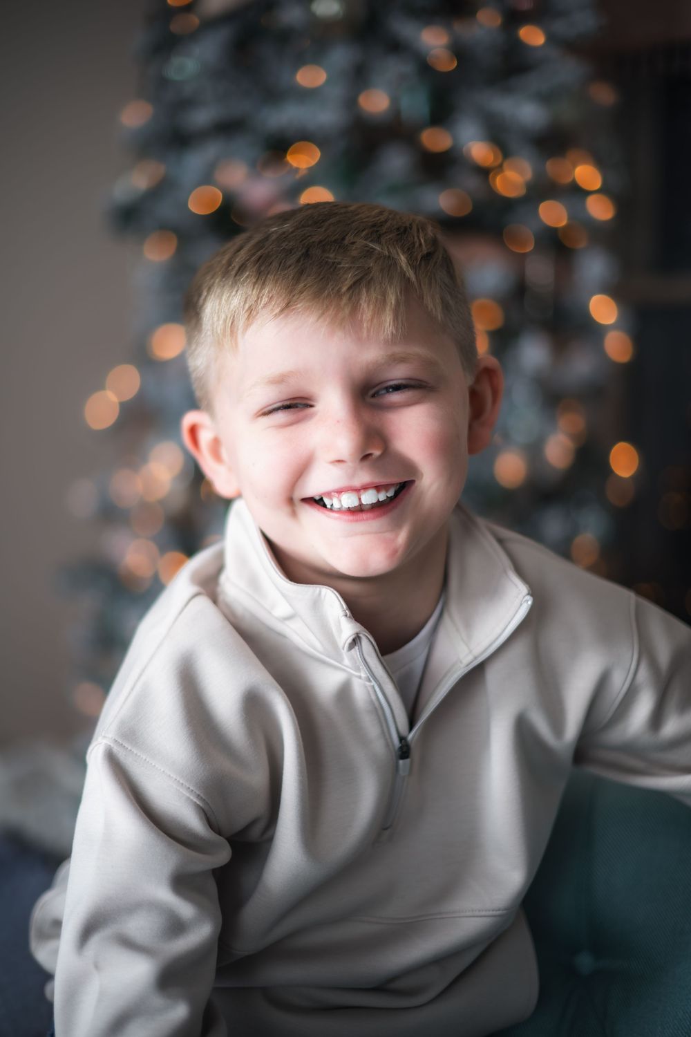 A child in a light gray sweatshirt smiles warmly against a background of soft, blurred holiday lights.
