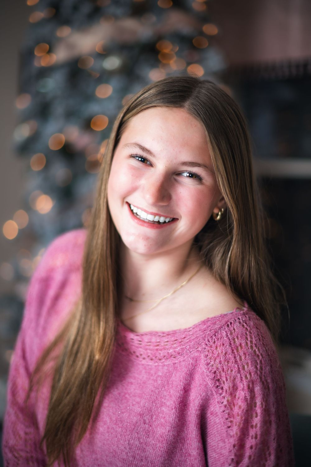 Portrait with festive bokeh background wearing a pink sweater and natural long hair.