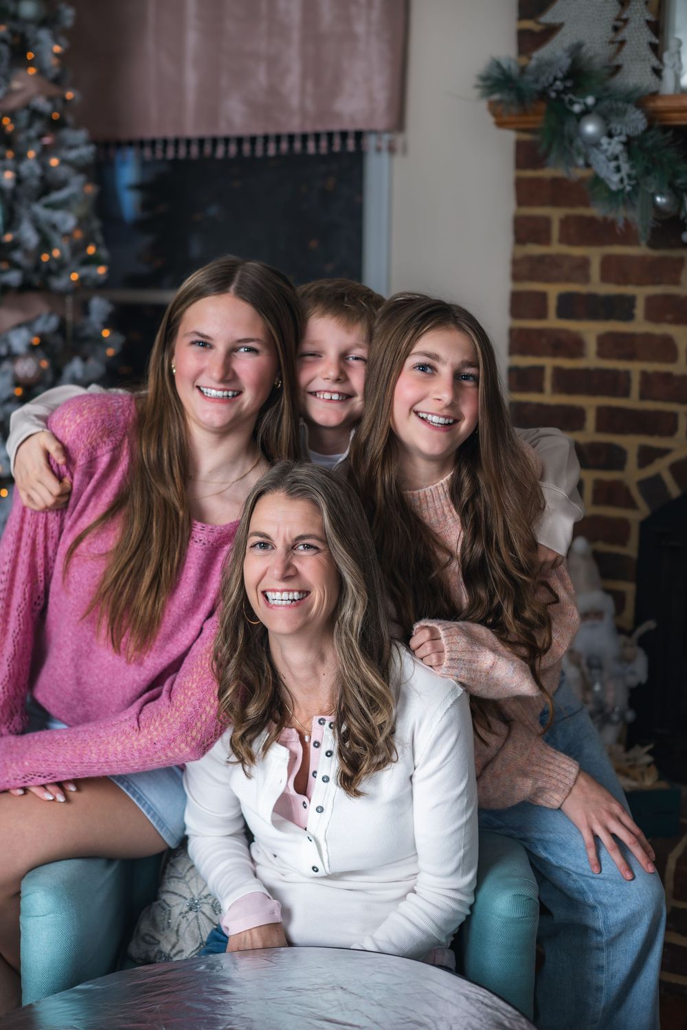 Four people laughing together on a blue couch during a holiday photoshoot with a Christmas tree in background.