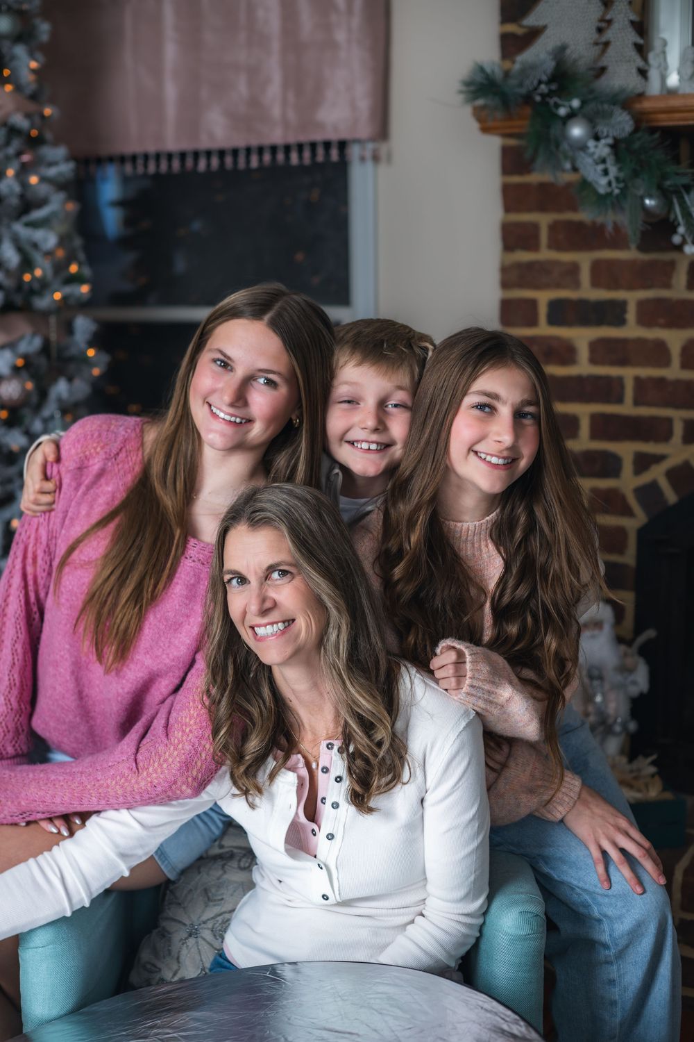 A family group sits together smiling on a couch during the holiday season with Christmas decorations in the background.