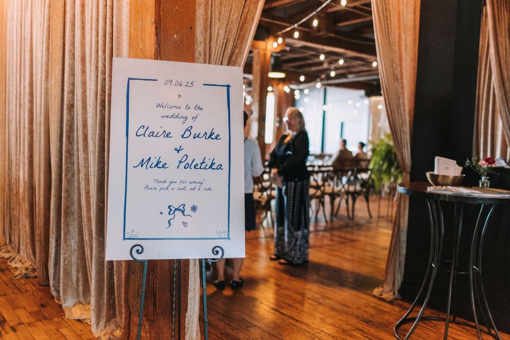 A panoramic view of an elegant event space with wooden floors, white drapes, and handwritten signs on display.