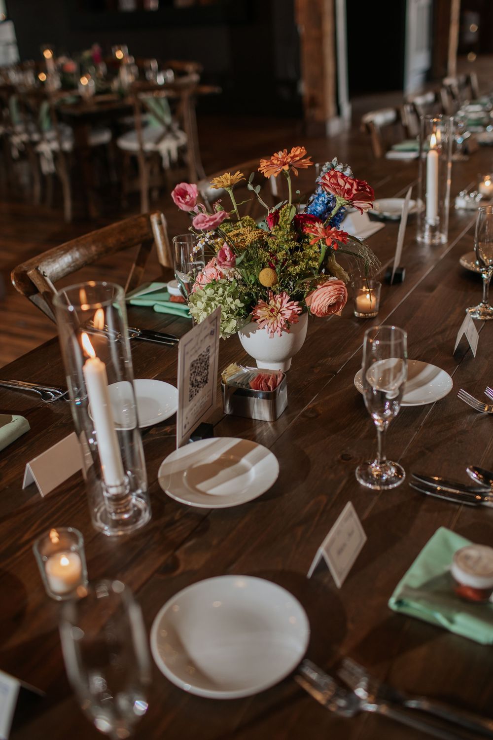 Elegant wedding reception table setting with white plates, mint napkins, and floral centerpieces on dark wooden tables.