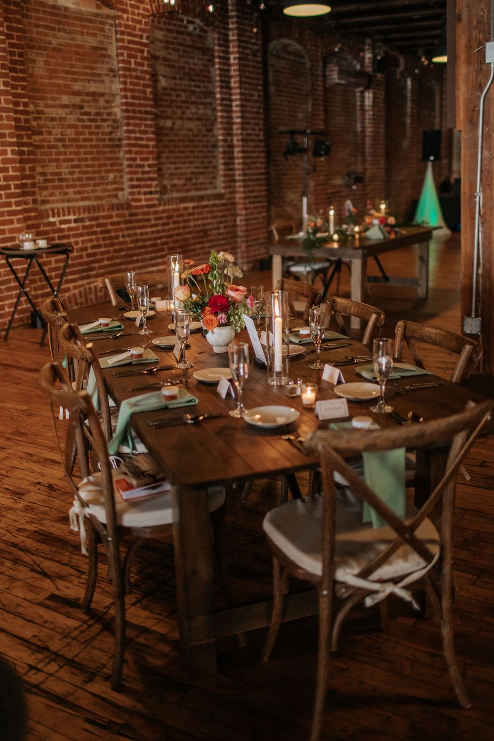Rustic wedding reception tables with floral centerpieces and place settings in a brick-walled industrial venue.