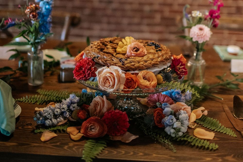 Wedding reception table decorated with colorful floral arrangements, pink and blue blooms, and rustic wooden details.