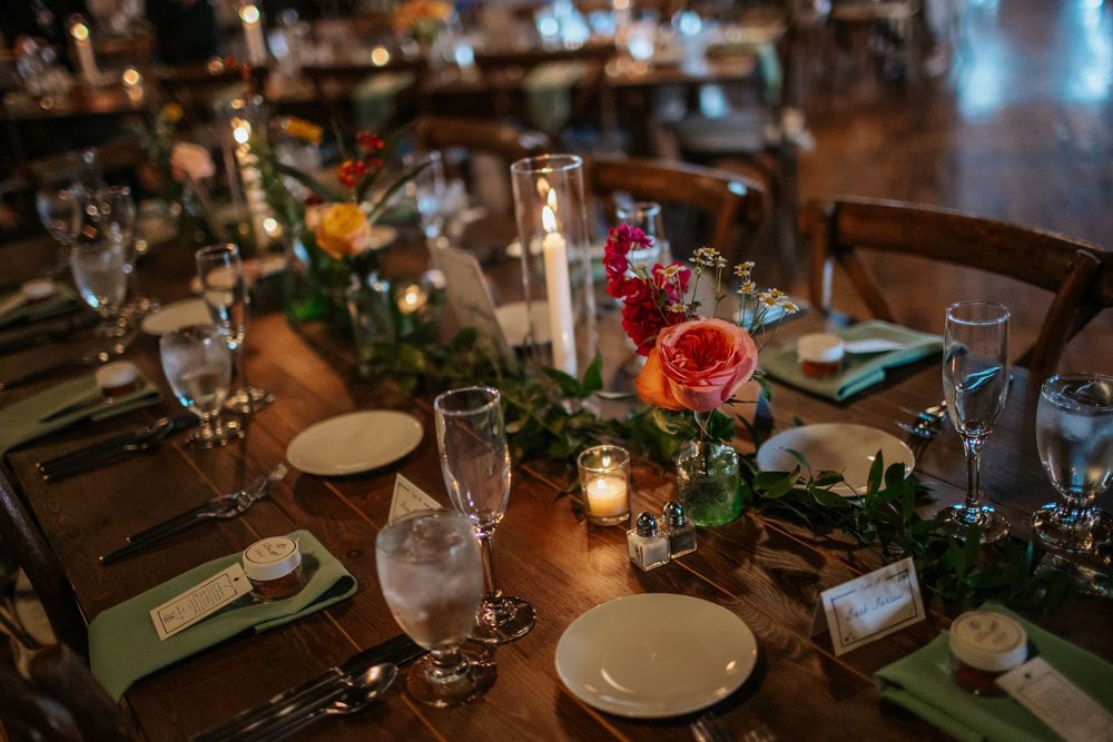 Elegant wedding reception tables decorated with greenery, candles, and place settings in a dimly lit venue.