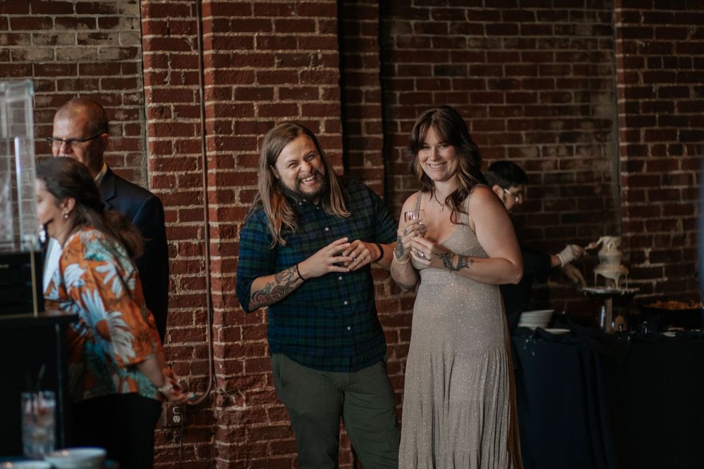 Wedding celebration in a brick-walled venue with guests mingling and laughing together.