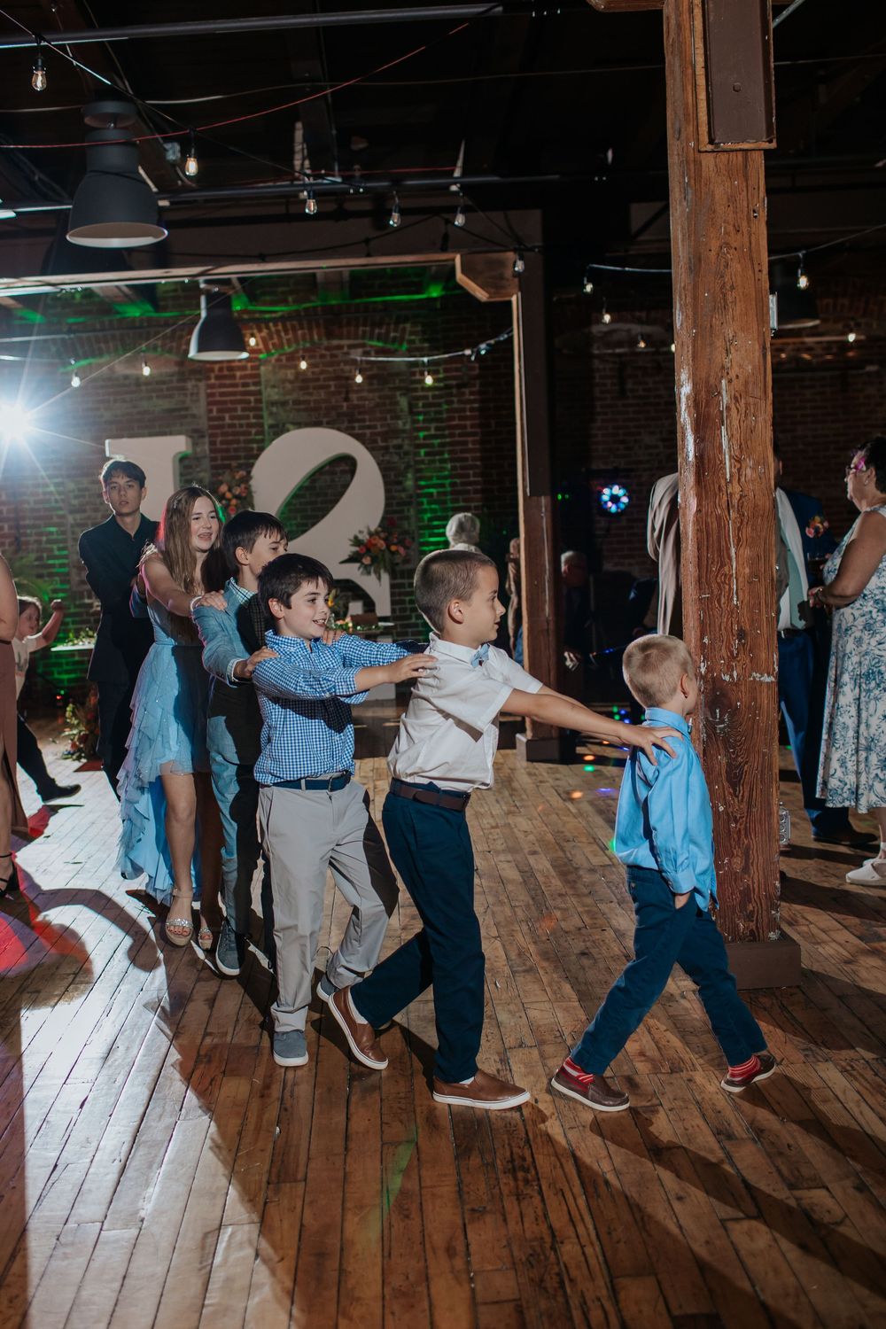 People dancing and having fun on a wooden floor in a rustic venue with exposed brick walls and string lights.