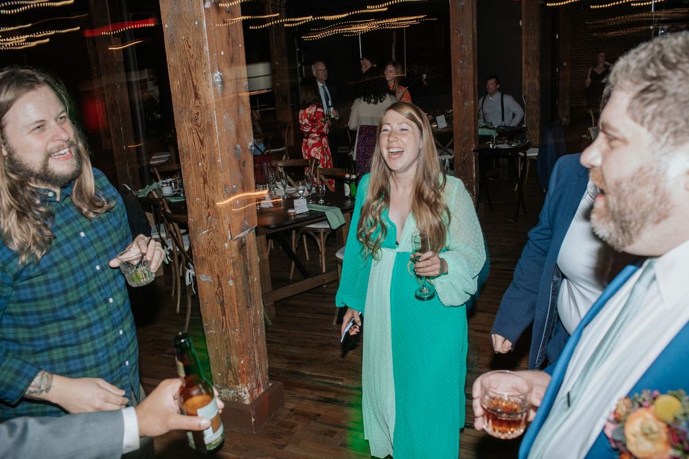 Guests enjoying drinks and conversation at an evening event in a rustic indoor space.