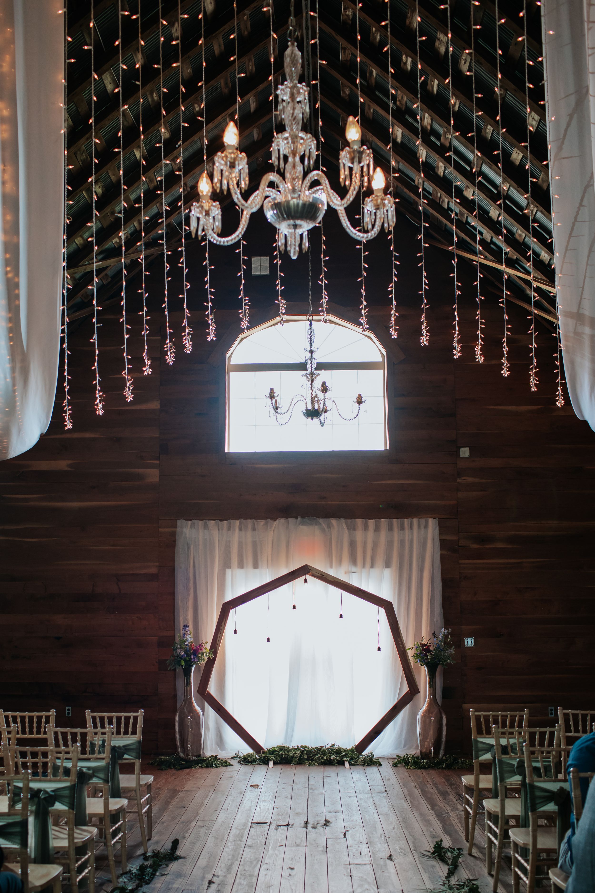 Rustic barn wedding venue decorated with twinkling lights and crystal chandeliers.