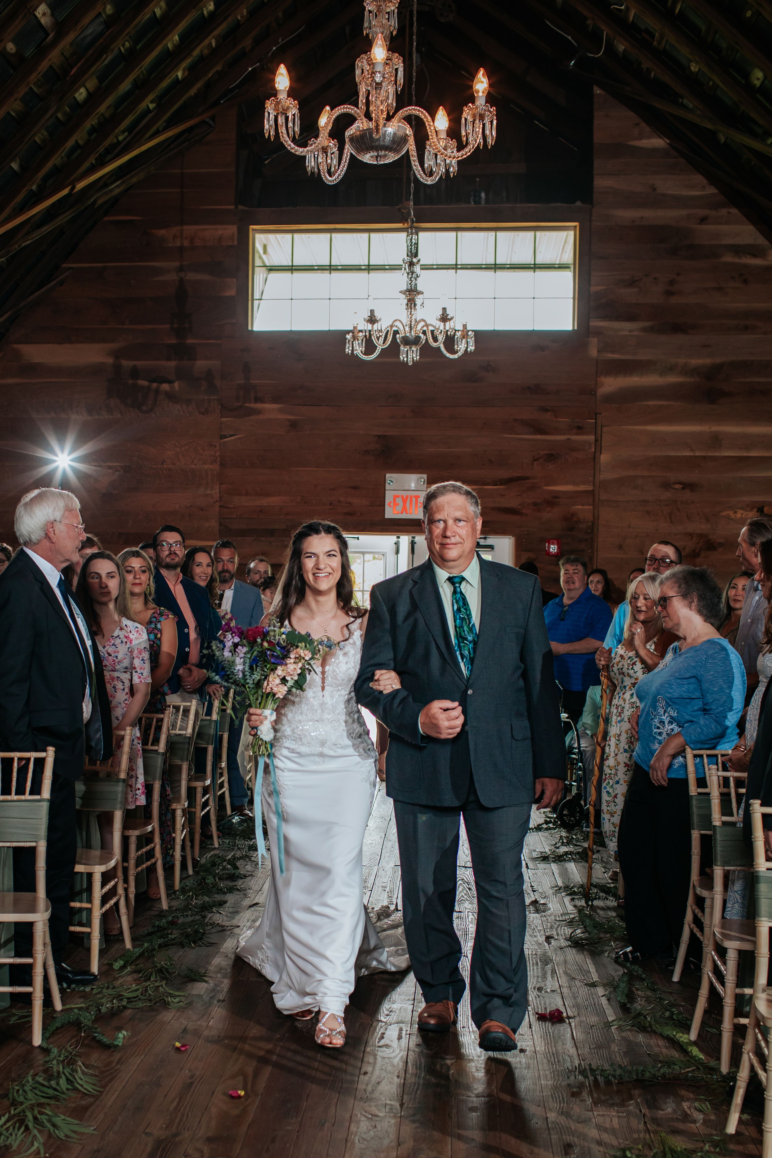 Wedding processional in rustic barn venue with elegant lighting and wooden details.