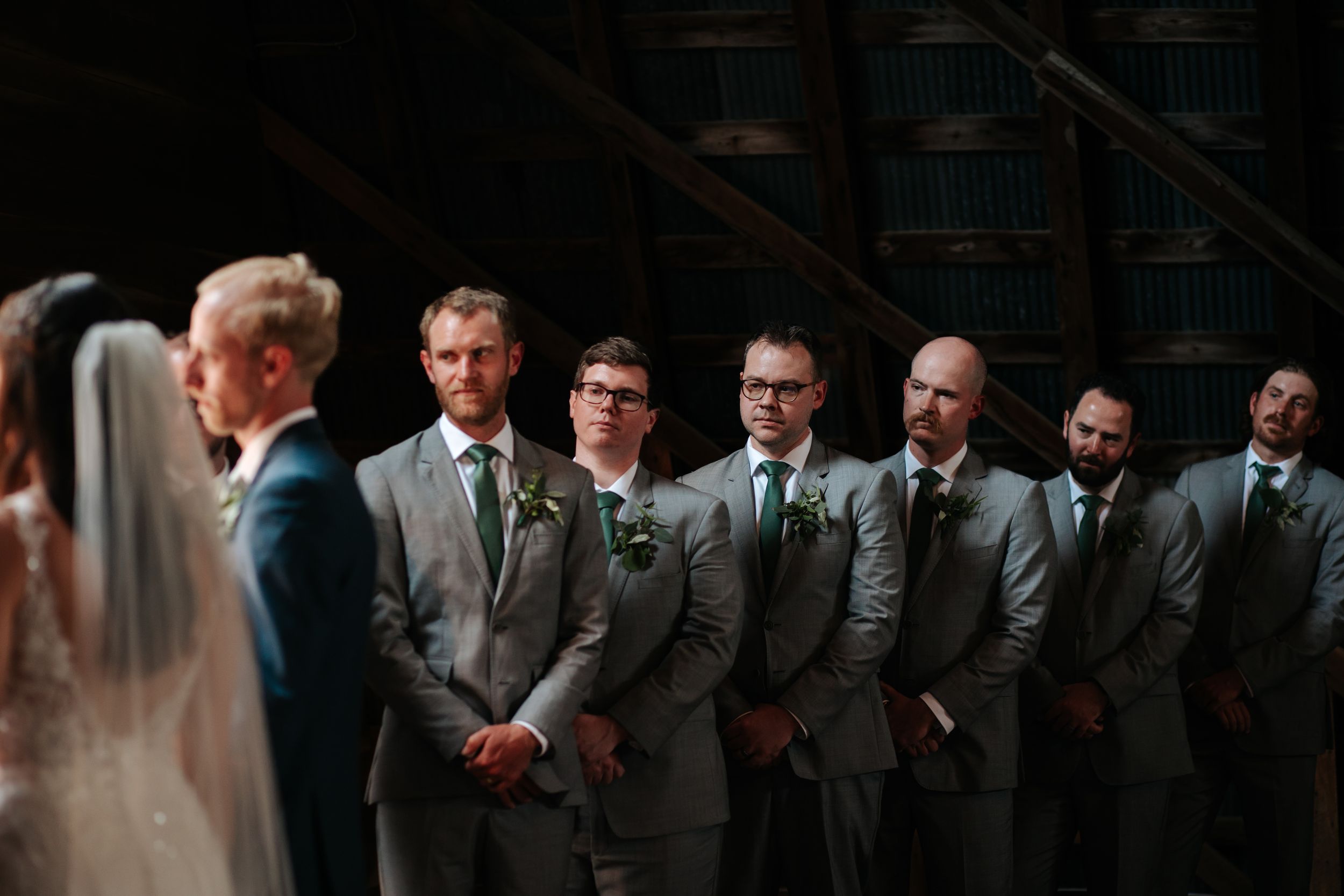 Groomsmen in formal suits lined up against dark background at wedding ceremony.