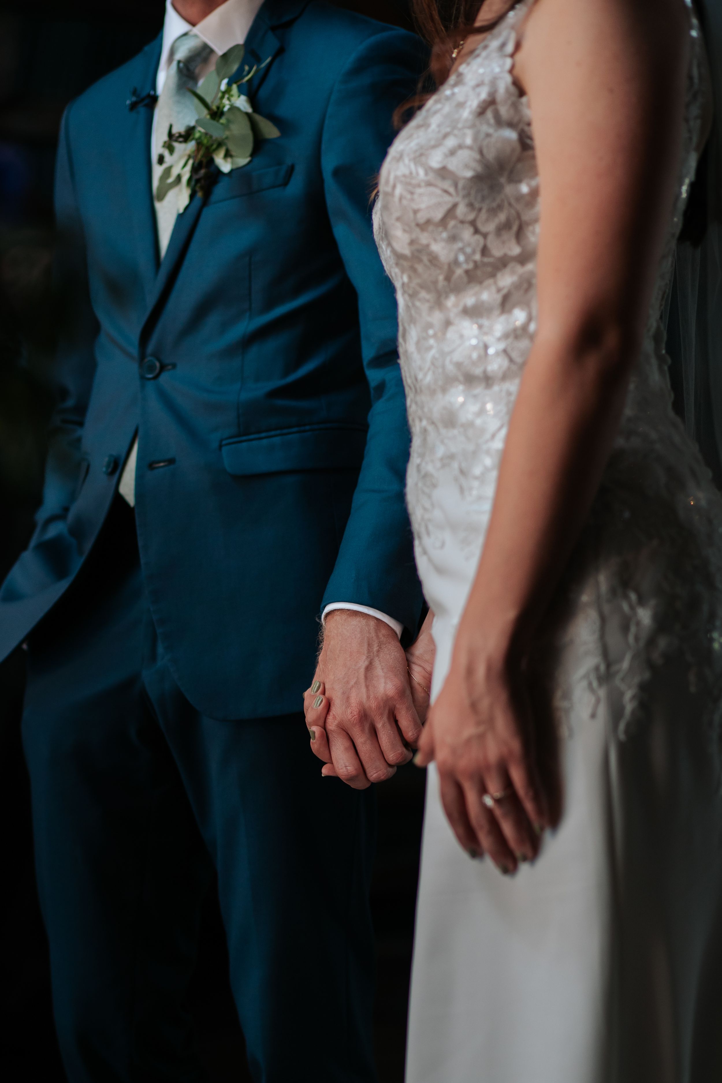 Close-up of wedding attire showing navy blue suit jacket next to white lace wedding dress.