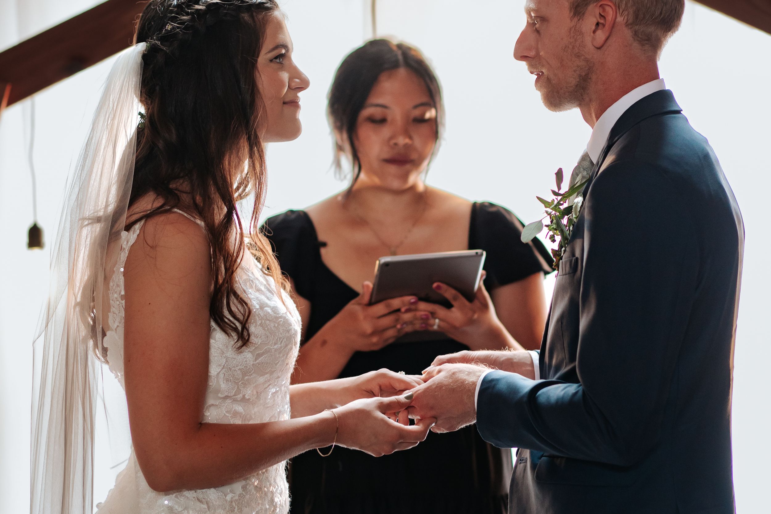 Ring exchange ceremony during indoor wedding with soft window lighting.