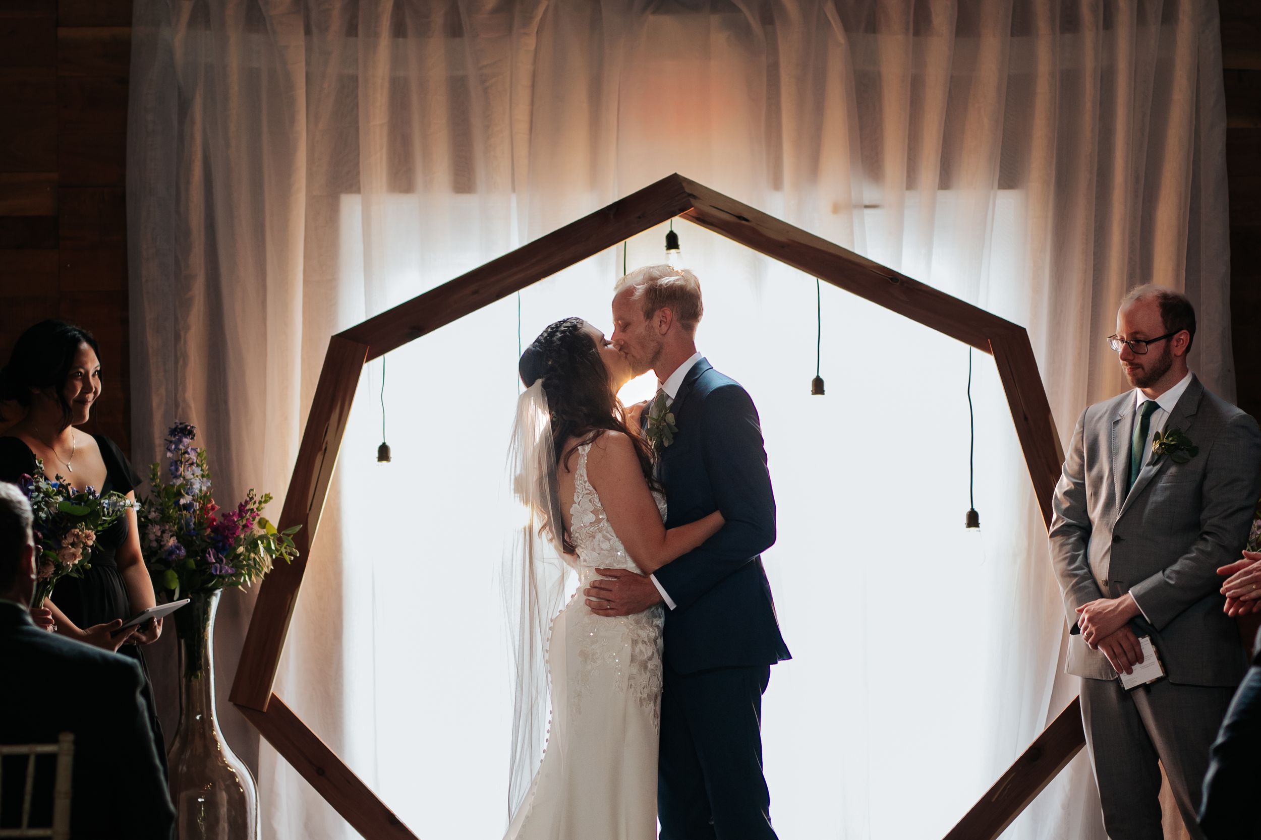 Wedding ceremony in rustic venue with draped fabric and pendant lighting creating romantic atmosphere.