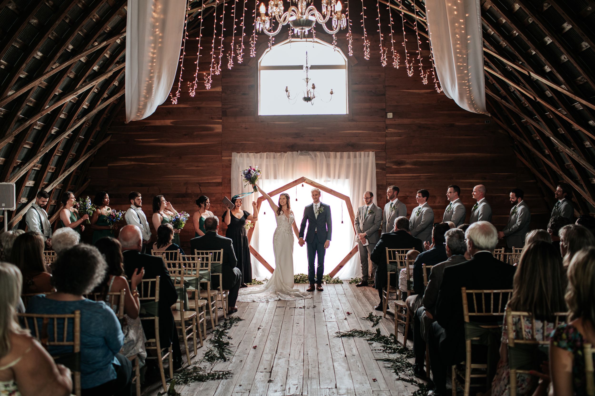 Wide view of barn wedding ceremony with wooden beams and white draping.