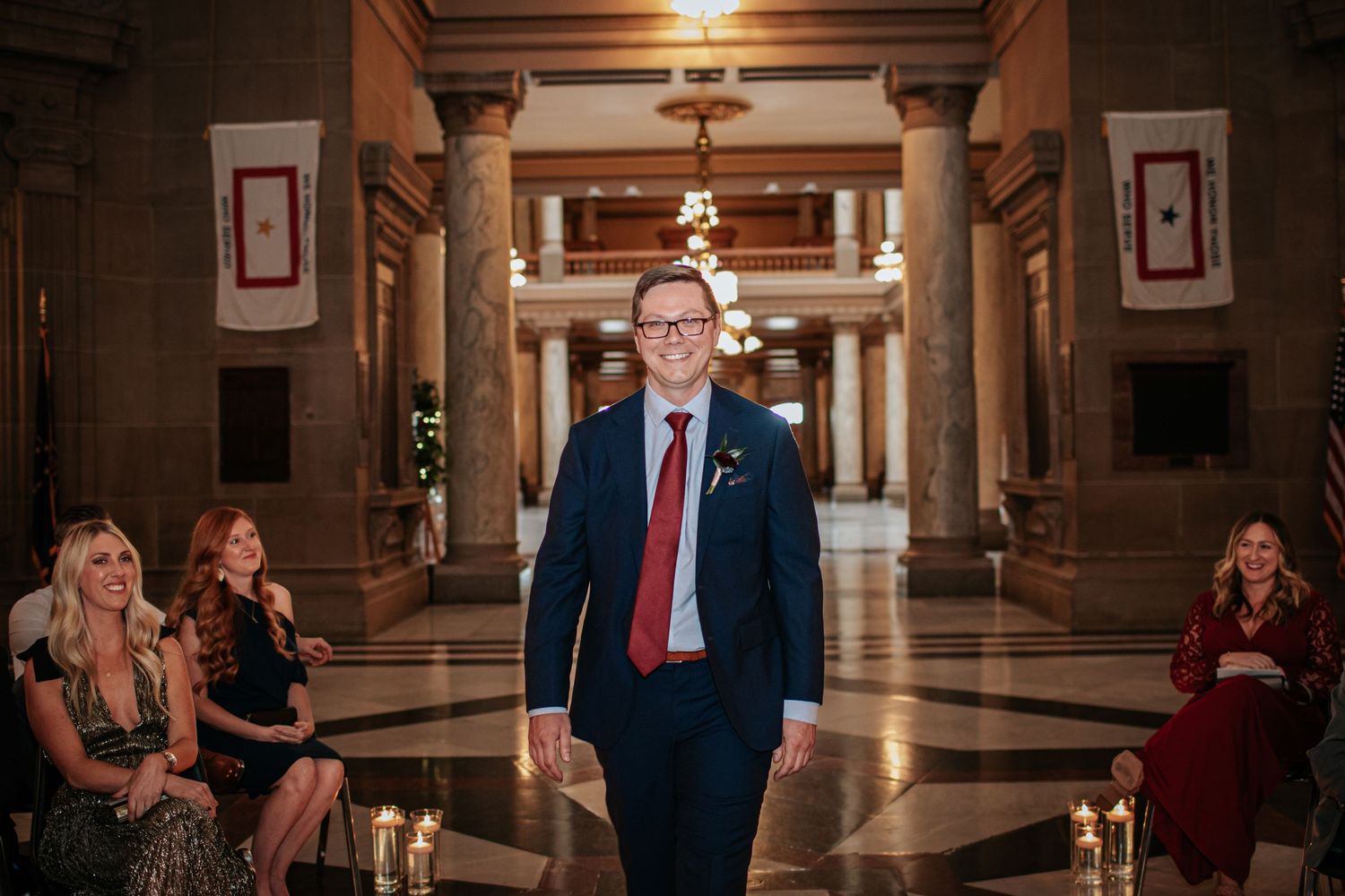 A romantic first look moment unfolds in an elegant hallway with ornate columns and warm lighting.